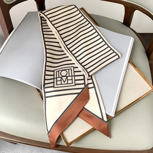 Detail of white striped skinny scarf with contrast tips and geometric logo on a magazine