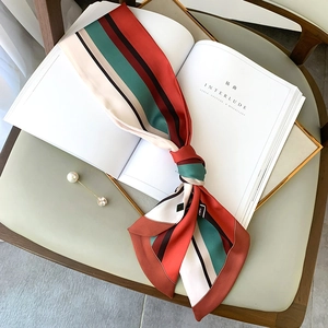 Detail of striped silk scarf tied on a book with pearl brooch on a green chair