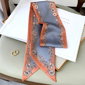 Détail d'un foulard étroit à imprimé floral rouge brique et bleu posé sur un magazine