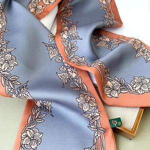 Détail d'un foulard en soie à fleurs gris-bleu avec bords orange et étiquette de marque
