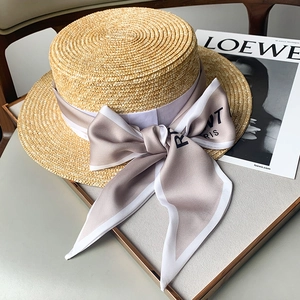 Detalle de un sombrero de paja de copa plana con un lazo de seda elegante con letras