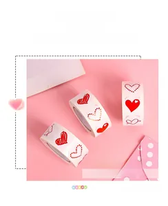 Macro shot of three heart-shaped sticker rolls with various red designs on pink envelopes