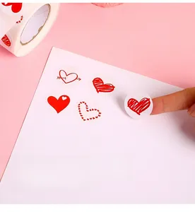 Close-up of hand peeling a heart sticker from a roll onto a white card surface