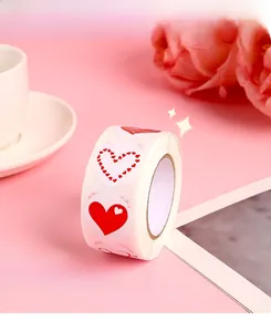 Detail of red heart roll stickers on pink background with white cup and floral decor