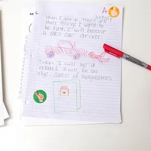 Detailansicht von Schüler-Aufsatzpapier mit Belohnungsaufklebern und rotem Stift