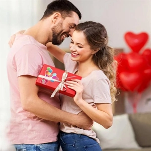 Woman holding red gift box with gold ribbon and heart balloons for Valentine's Day