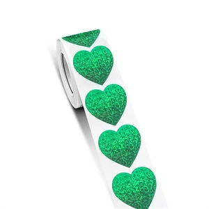 Macro shot of roll-packed sparkling holographic green heart-shaped adhesive stickers
