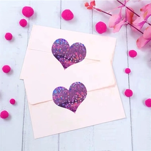 Macro detail of a purple laser heart sticker sealing a white envelope on a wood background