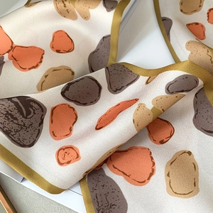Detail of silk scarf featuring abstract pebble stone prints and fine gold stitched edges