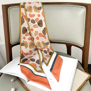 Narrow silk scarf with pebble geometric patterns on a wooden chair with pearl accessory