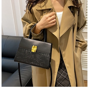 Detail view of black crocodile pattern bag with gold hardware worn by model