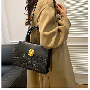 Detail of black crocodile texture handbag with gold metal clasp on tan trench coat