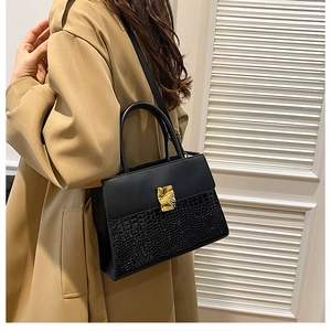 Detail of black crocodile texture handbag with golden buckle on elegant camel trench coat