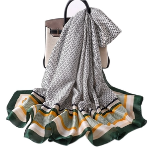 Women's silk scarf with geometric Y-pattern and green stripe border draped on a handbag