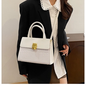 Detail of white crocodile embossed handbag with gold metal lock held by a model