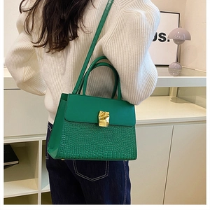Close-up of emerald green crocodile texture handbag worn by a model in a modern room
