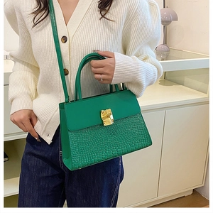 Detail of dark green crocodile pattern handbag with gold clasp and textured flap