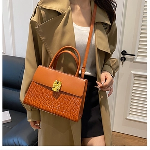 Detail of crocodile embossed crossbody bag with golden metal lock and leather strap