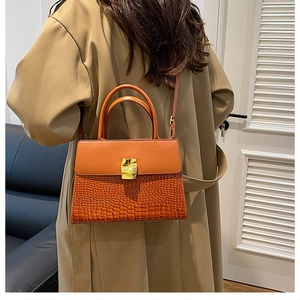 Detail view of a brown faux-crocodile texture handbag with a gold metal lock on a model