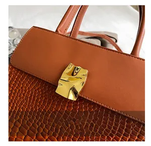 Detail of caramel brown croc-embossed leather with wavy golden metal buckle on a handbag