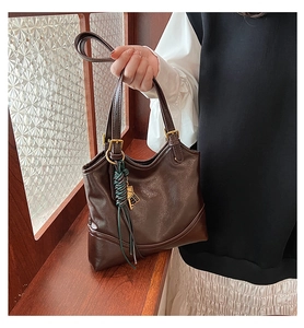 Detail view of coffee brown faux leather tote with vintage metal buckle and fringe charm
