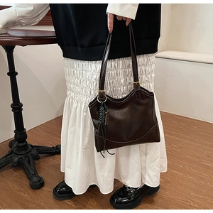 Detail of dark brown leather tote with golden hardware buckle and woven tassel charm