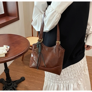 Detail of dark brown vintage oil wax leather tote bag with unique green braided charm
