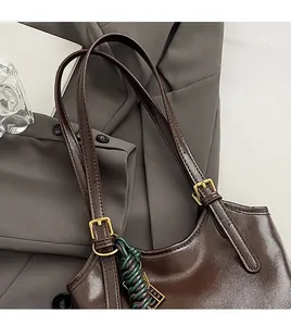 Detail of dark brown leather strap with golden buckle and metallic F charm on tote bag