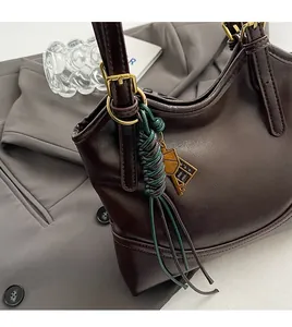 Detail of oil wax leather tote bag featuring green woven charm and golden key hardware