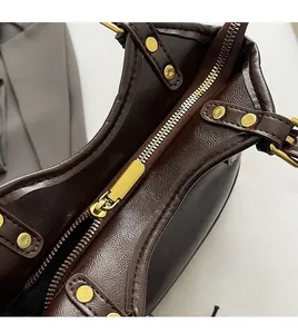 Close-up of smooth gold metal zipper and textured dark brown leather on underarm bag