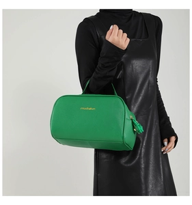 Close-up of green pebble leather Boston bag with gold logo and stylish tassel detail