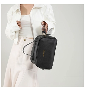 Détail d'un sac à main en cuir grainé noir avec logo doré porté par un mannequin