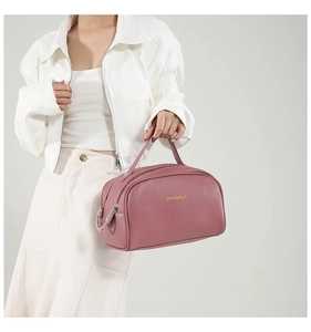 Modèle tenant une trousse de maquillage en cuir PU rose avec logo doré et double zip