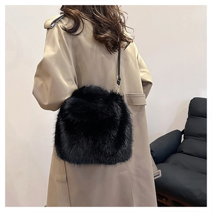 Detail of a fluffy black faux fur bucket bag with a slim leather strap and gold buckle