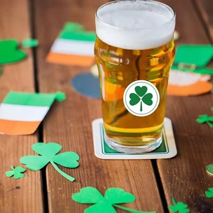 Saint Patrick's Day glass beer mug with green shamrock logo on dark wooden table