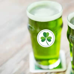 St. Patrick's Day green beer glass with shamrock sticker on light wood background
