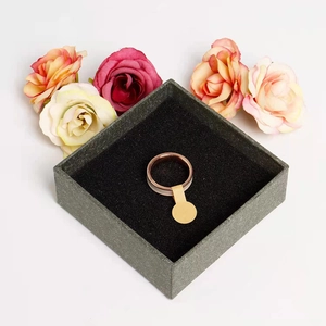 Rose gold metal and white ceramic ring with a round gold tag on black display box