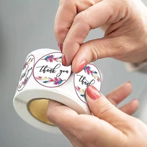 Colorful feather Thank You stickers being peeled from a roll for gift packaging