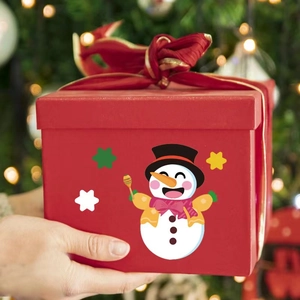 Christmas gift box with snowman pattern and red velvet bow held against festive lights