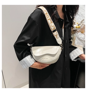Detail of cream saddle bag with wide printed strap and fashion logo on the flap