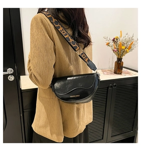 Detail of black glossy saddle bag with vintage jacquard strap on a female model