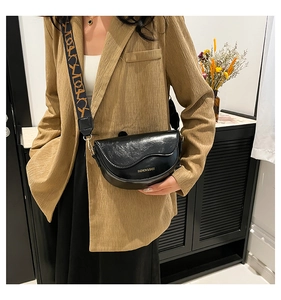 Detail of black leather saddle bag featuring a wide patterned strap on a stylish model