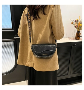 Detail of black crescent saddle bag with patterned wide strap and golden lettering