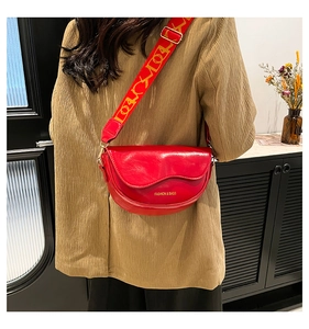 Detail of red crescent leather bag featuring a gold fashion logo and a woven strap