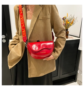 Detail of red saddle bag featuring glossy leather texture and stylish jacquard wide strap