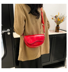 Close-up of red semi-circle saddle bag with wide patterned strap and glossy finish