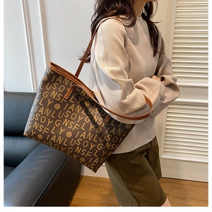 Detailed view of large printed tote bag with leather straps and repeated letter pattern
