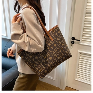 Close-up of a large tote bag with letter prints and brown leather shoulder straps