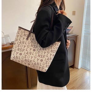Detail shot of large tote bag with brown letter prints and leather handles on a suit