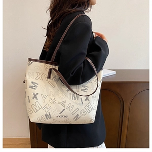Detail of off-white tote bag with black lettering and brown leather handle on shoulder
